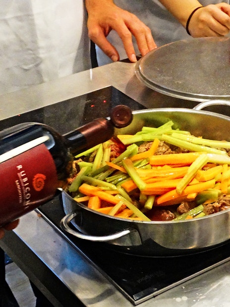 Cooking class participants preparing a dish with vegetables and wine in Florence.