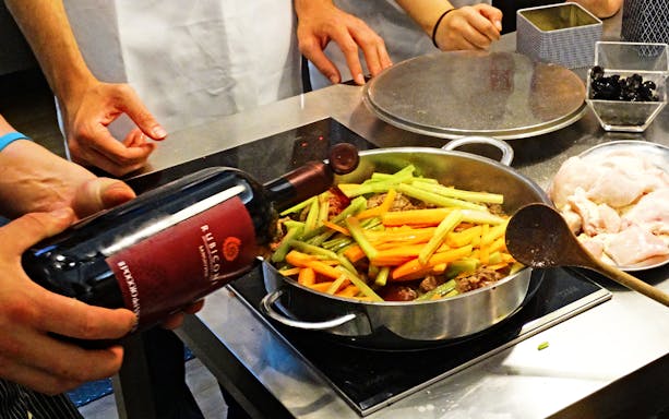 Cooking class participants preparing a dish with vegetables and wine in Florence.