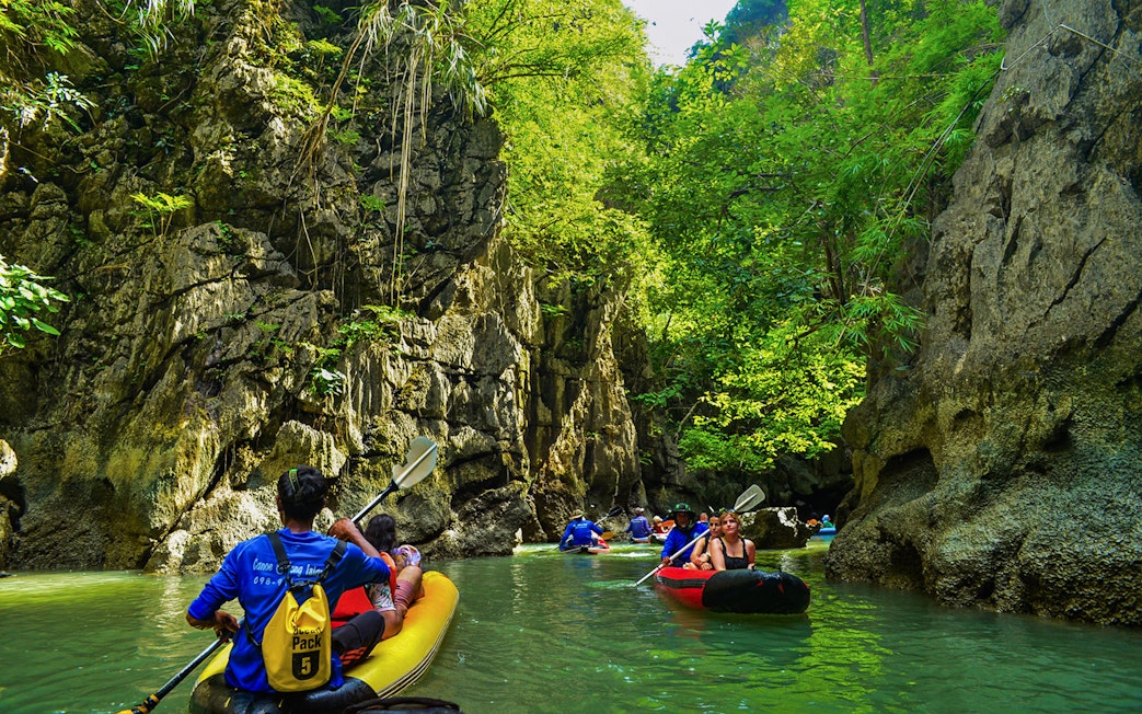 Tourists kayaking through limestone cliffs at Phang Nga Bay, Thailand.