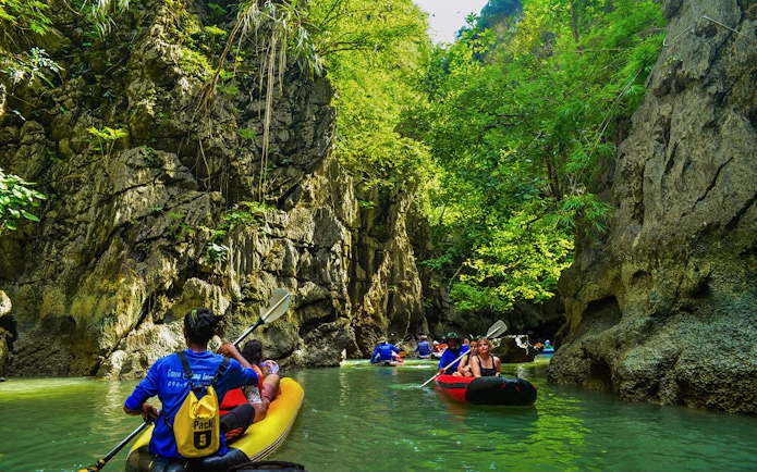 Tourists kayaking through limestone cliffs at Phang Nga Bay, Thailand.