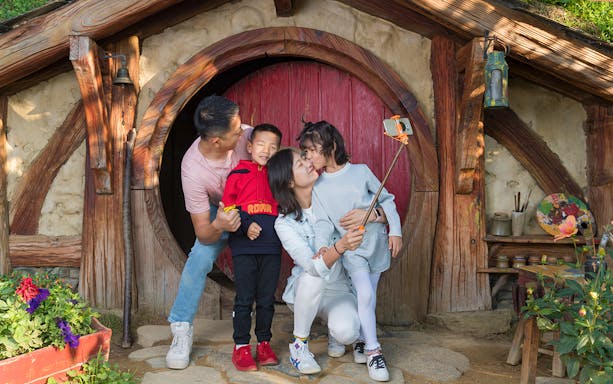 Family taking selfie at Hobbiton Movie Set entrance, Auckland tour.