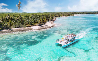 Catamaran sailing near palm-lined Saona Island coast in turquoise waters.