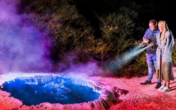 Visitors exploring Te Puia geysers at night with flashlight.