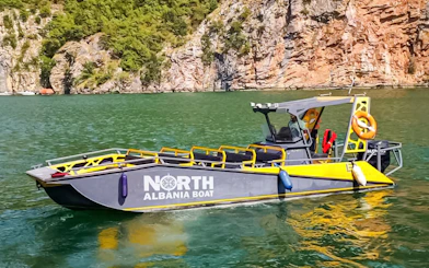 Boat on Komani Lake during day trip from Tirana, Albania, with rocky cliffs in background.