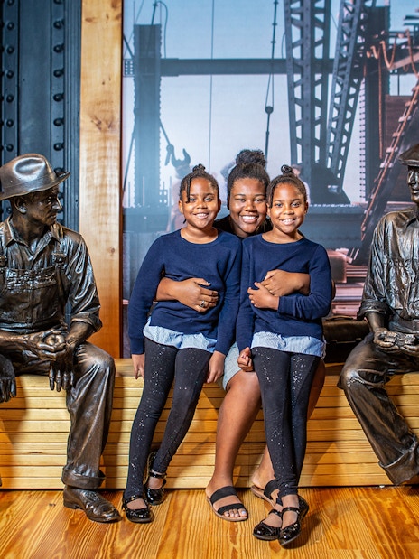 Family posing with construction worker statues at museum exhibit.
