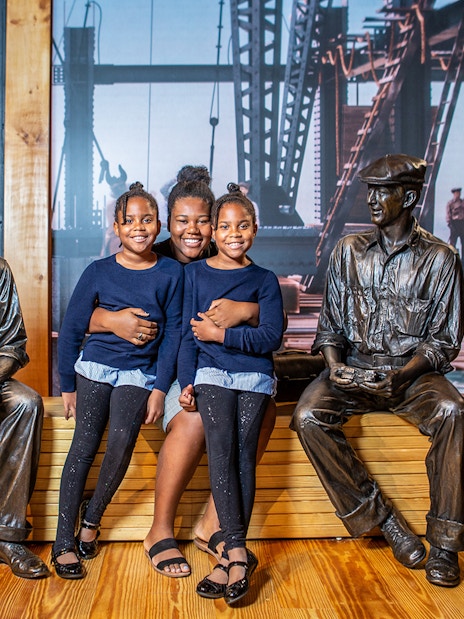 Family posing with construction worker statues at museum exhibit.