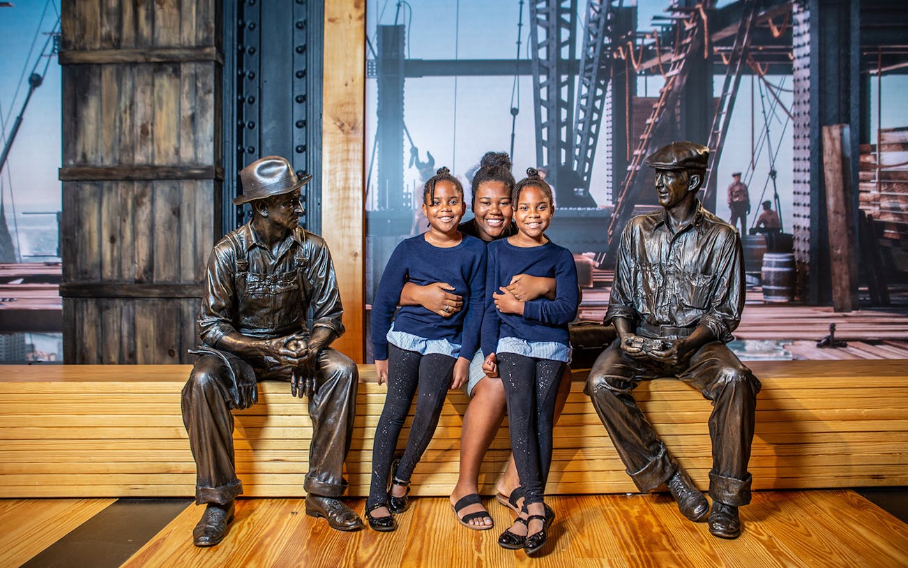Family posing with construction worker statues at museum exhibit.