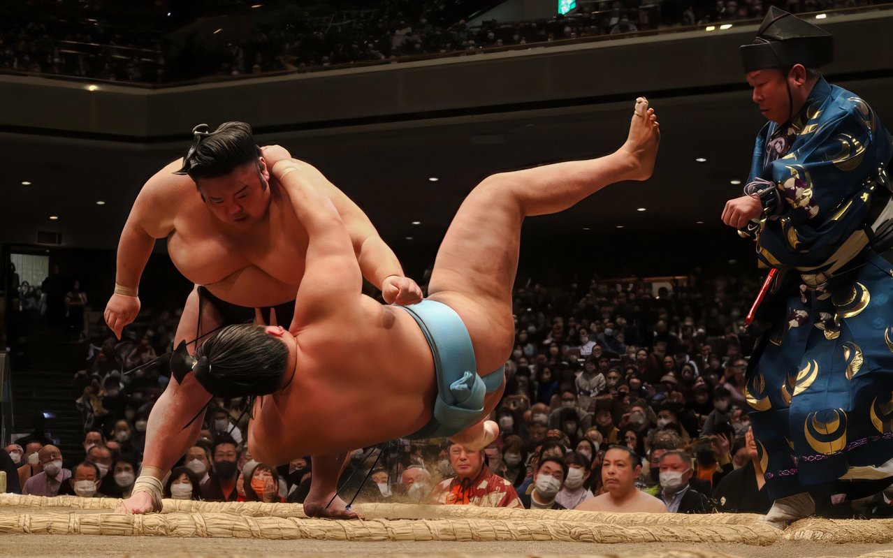 Sumo wrestler executing a move against opponent in a crowded arena.