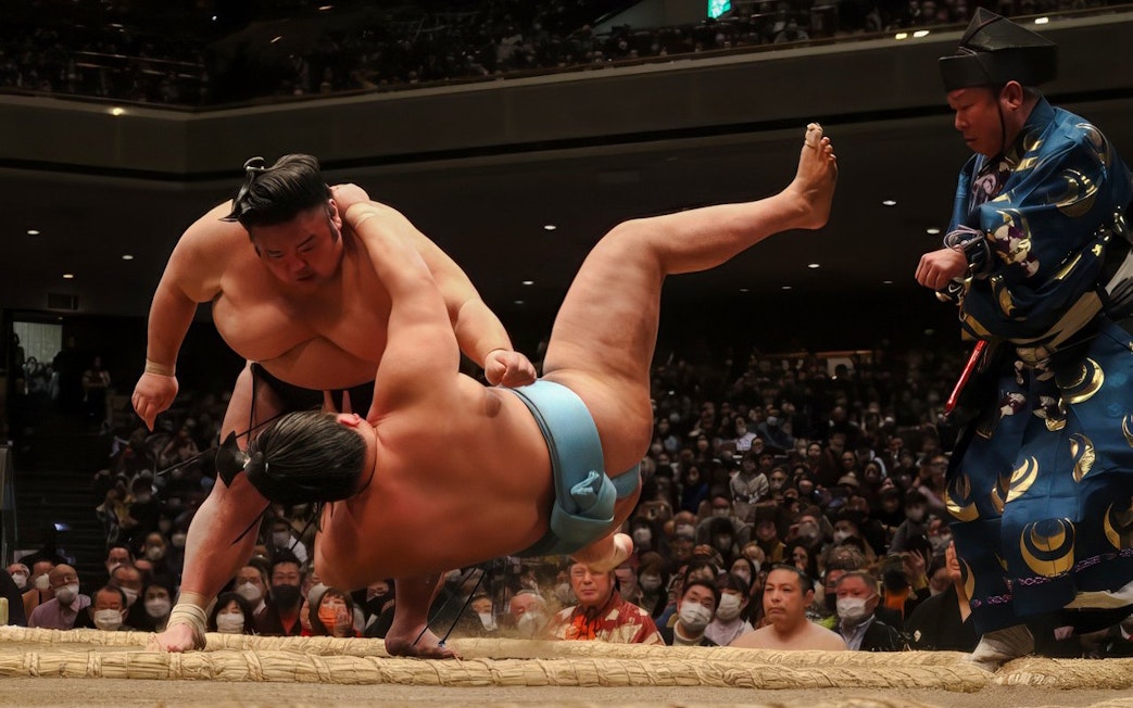 Sumo wrestler executing a move against opponent in a crowded arena.