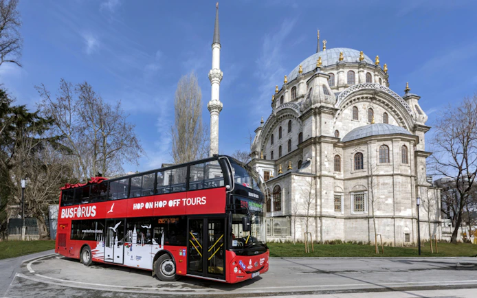 Red double-decker bus in front of a historic mosque on the Busforus Istanbul tour.