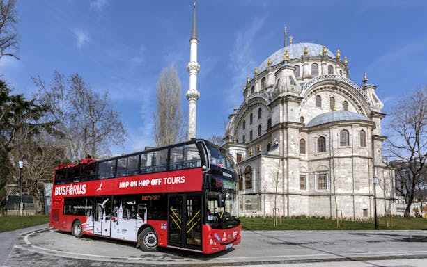 Red double-decker bus in front of a historic mosque on the Busforus Istanbul tour.
