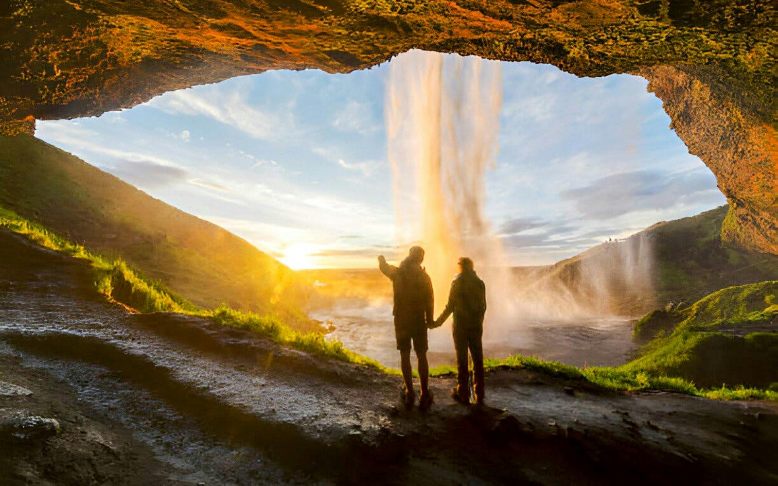 People exploring the cave behind Seljalandsfoss waterfall in Iceland at sunset.