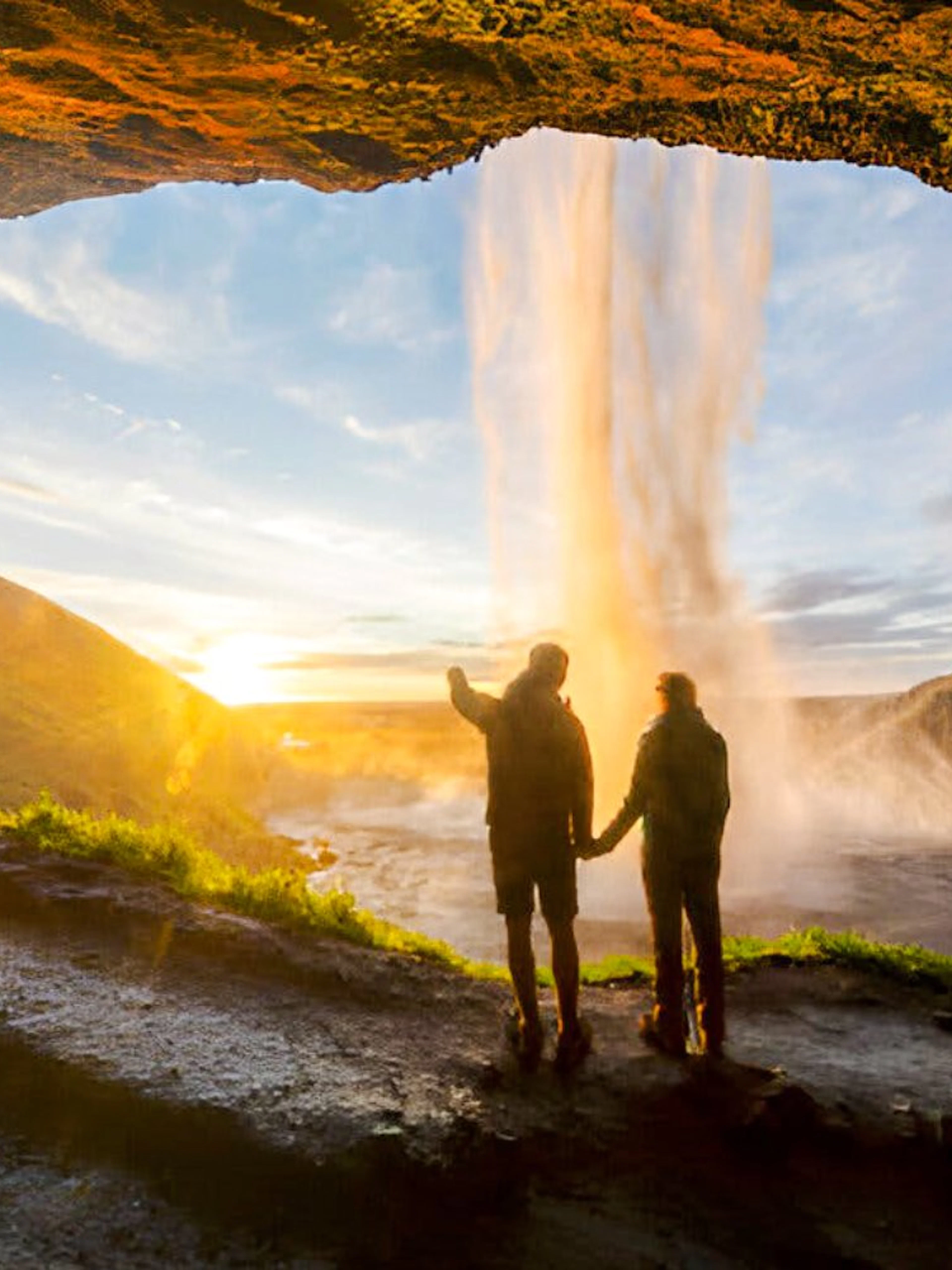 People exploring the cave behind Seljalandsfoss waterfall in Iceland at sunset.