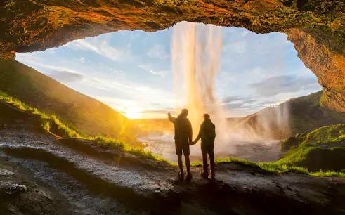 People exploring the cave behind Seljalandsfoss waterfall in Iceland at sunset.