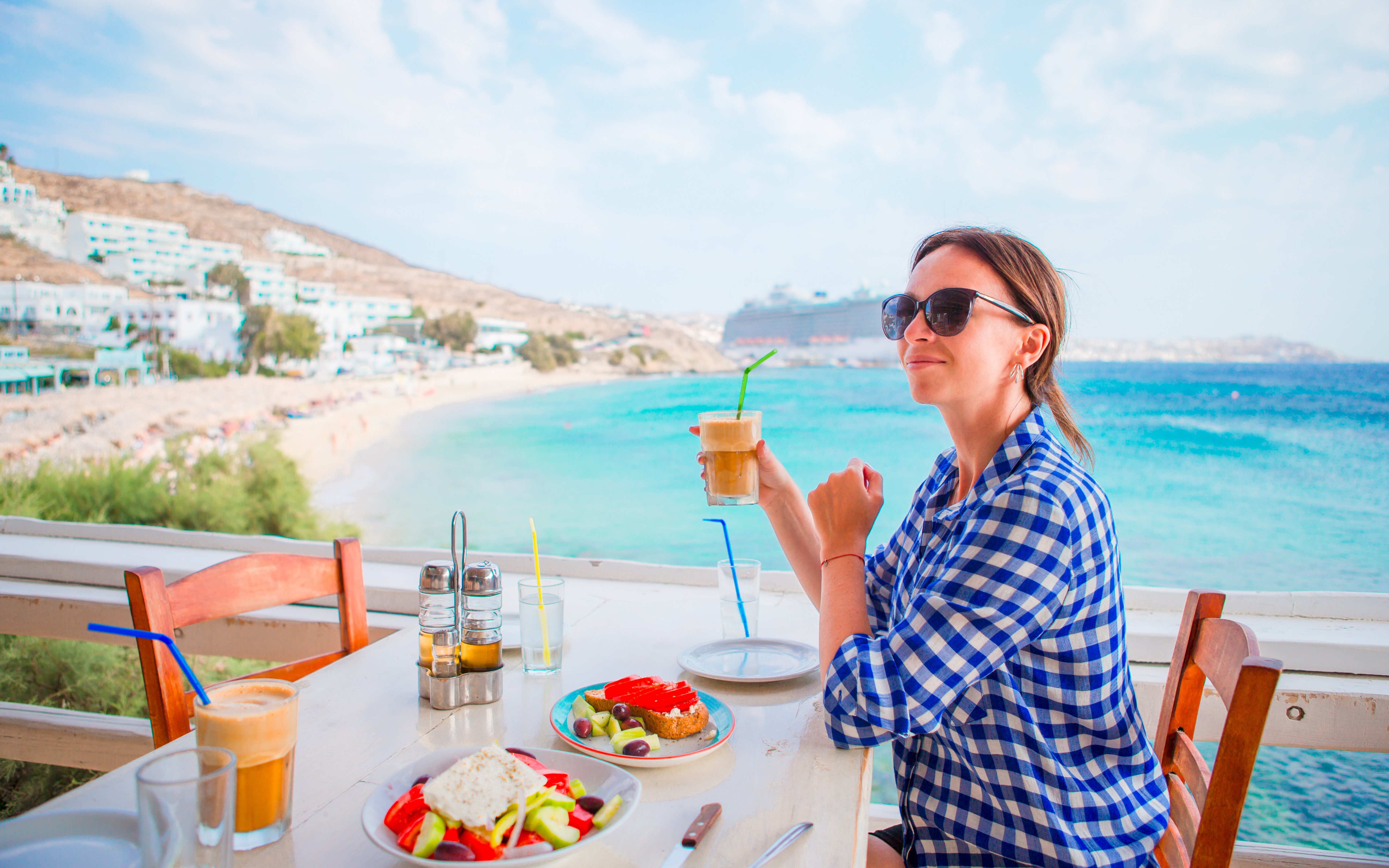 Woman enjoying Greek lunch by the sea in Mykonos, Greece.