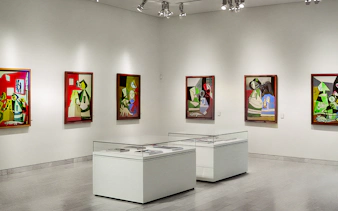 Picasso Museum interior with abstract paintings on white walls and display cases.