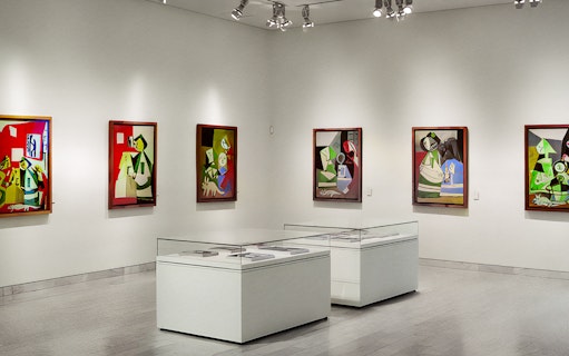 Picasso Museum interior with abstract paintings on white walls and display cases.