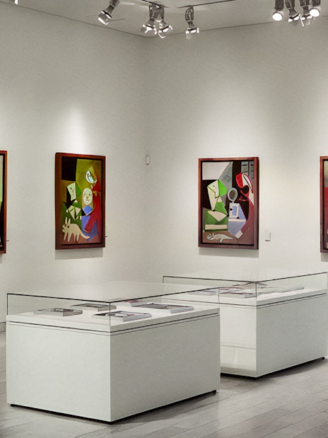 Picasso Museum interior with abstract paintings on white walls and display cases.