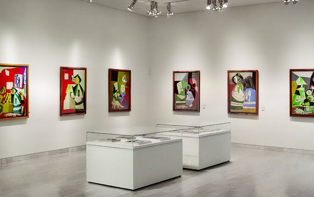 Picasso Museum interior with abstract paintings on white walls and display cases.