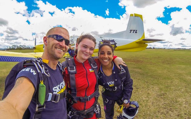 Skydivers preparing for tandem jump in Bay of Islands, New Zealand, with plane in background.