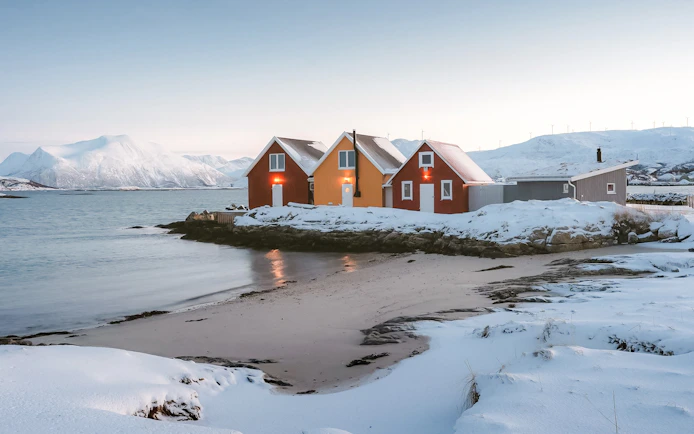 Colorful cabins by snowy Sommarøy Fjord, Tromsø, with mountains in the background.