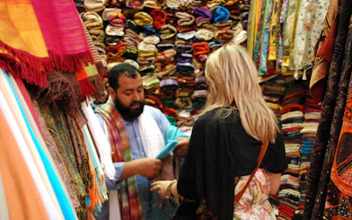 Shopkeeper showing colorful fabrics to a tourist in Fes souk.