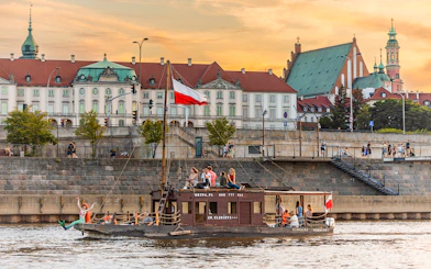 Tourists on a traditional Galar cruise on the Vistula River in Warsaw, Poland, with historic buildings in the background.