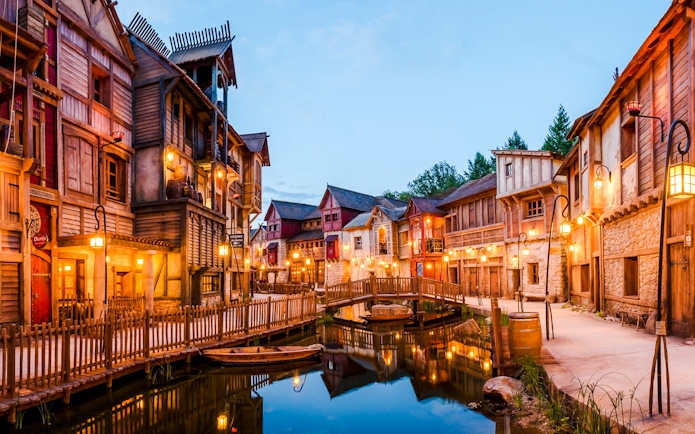Rustic village scene at Asterix Park with wooden buildings and a canal bridge.
