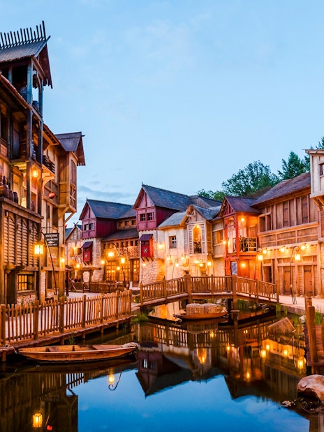 Rustic village scene at Asterix Park with wooden buildings and a canal bridge.