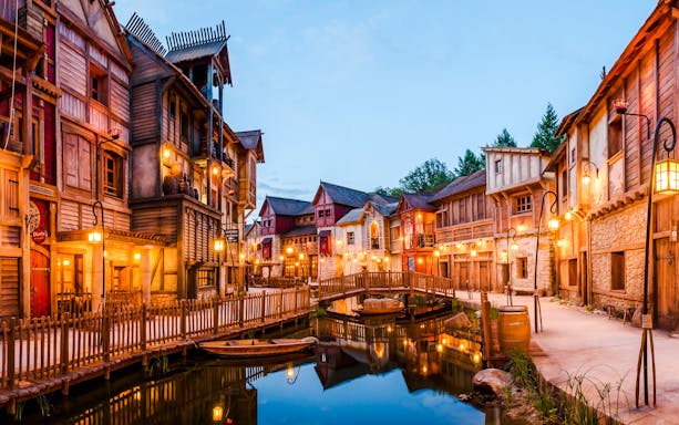 Rustic village scene at Asterix Park with wooden buildings and a canal bridge.