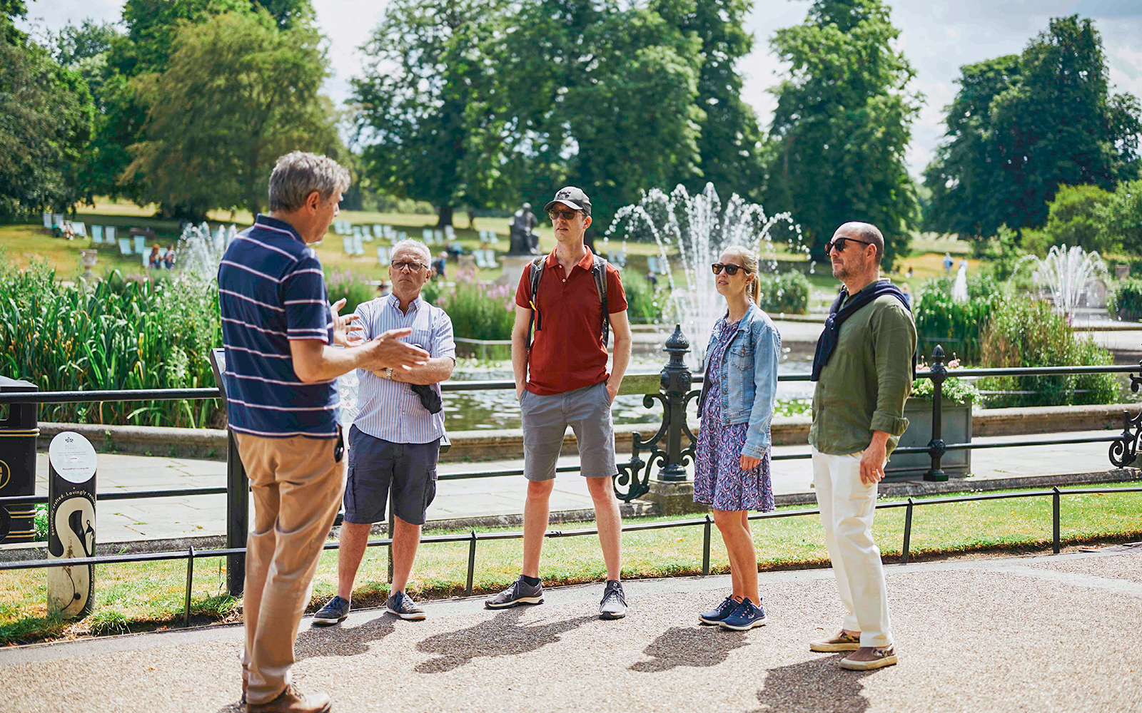 Group listening to a guide near fountains at Kensington Palace gardens.