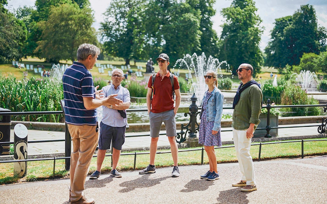Group listening to a guide near fountains at Kensington Palace gardens.