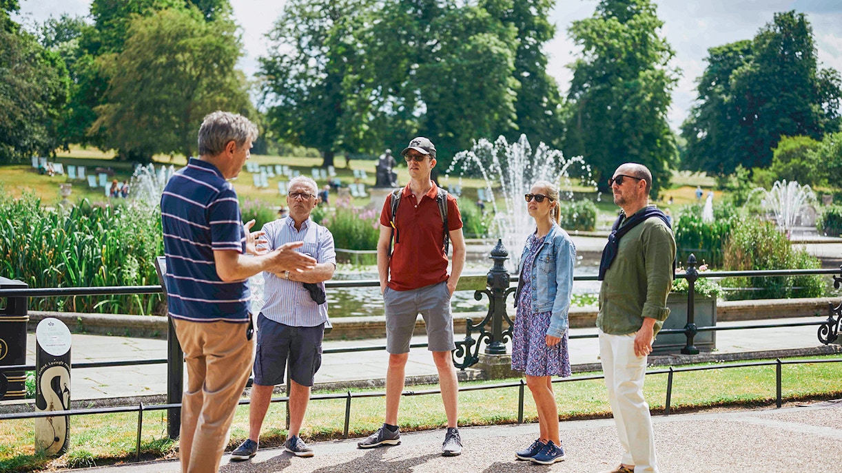 Group listening to a guide near fountains at Kensington Palace gardens.