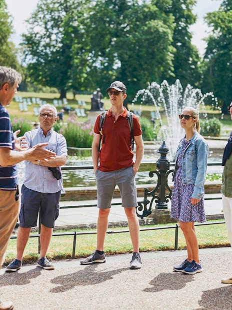 Group listening to a guide near fountains at Kensington Palace gardens.