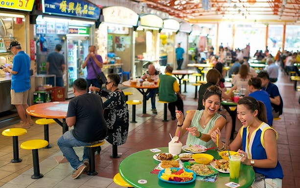 Visitors enjoying diverse dishes at a bustling Chinatown hawker center during a food tasting tour.