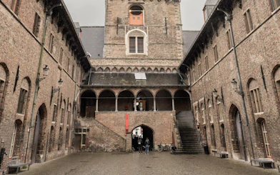 Courtyard view of Belfort tower in Bruges, Belgium, with arched windows and stone steps.