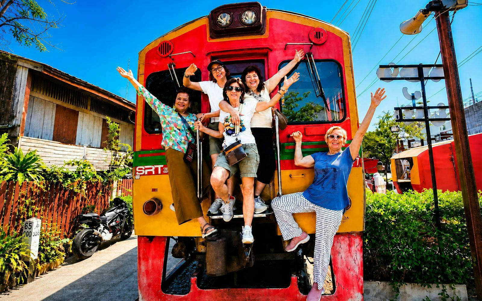 Tourists posing in front of a train at Maeklong Train Market, Thailand.