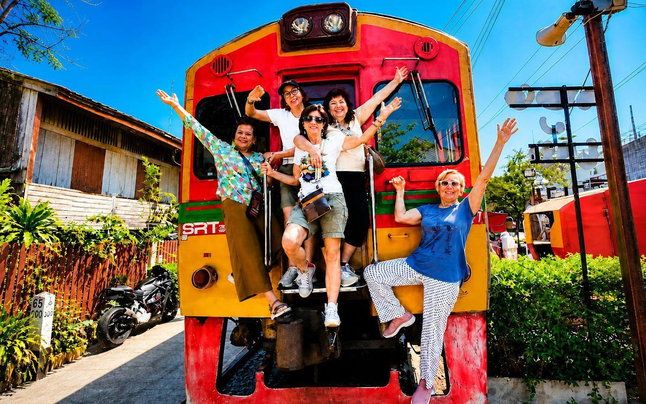 Tourists posing in front of a train at Maeklong Train Market, Thailand.