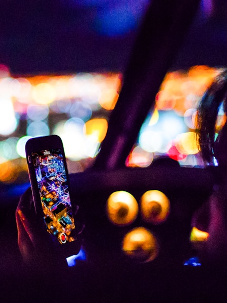 Person photographing city lights from helicopter cockpit at night.