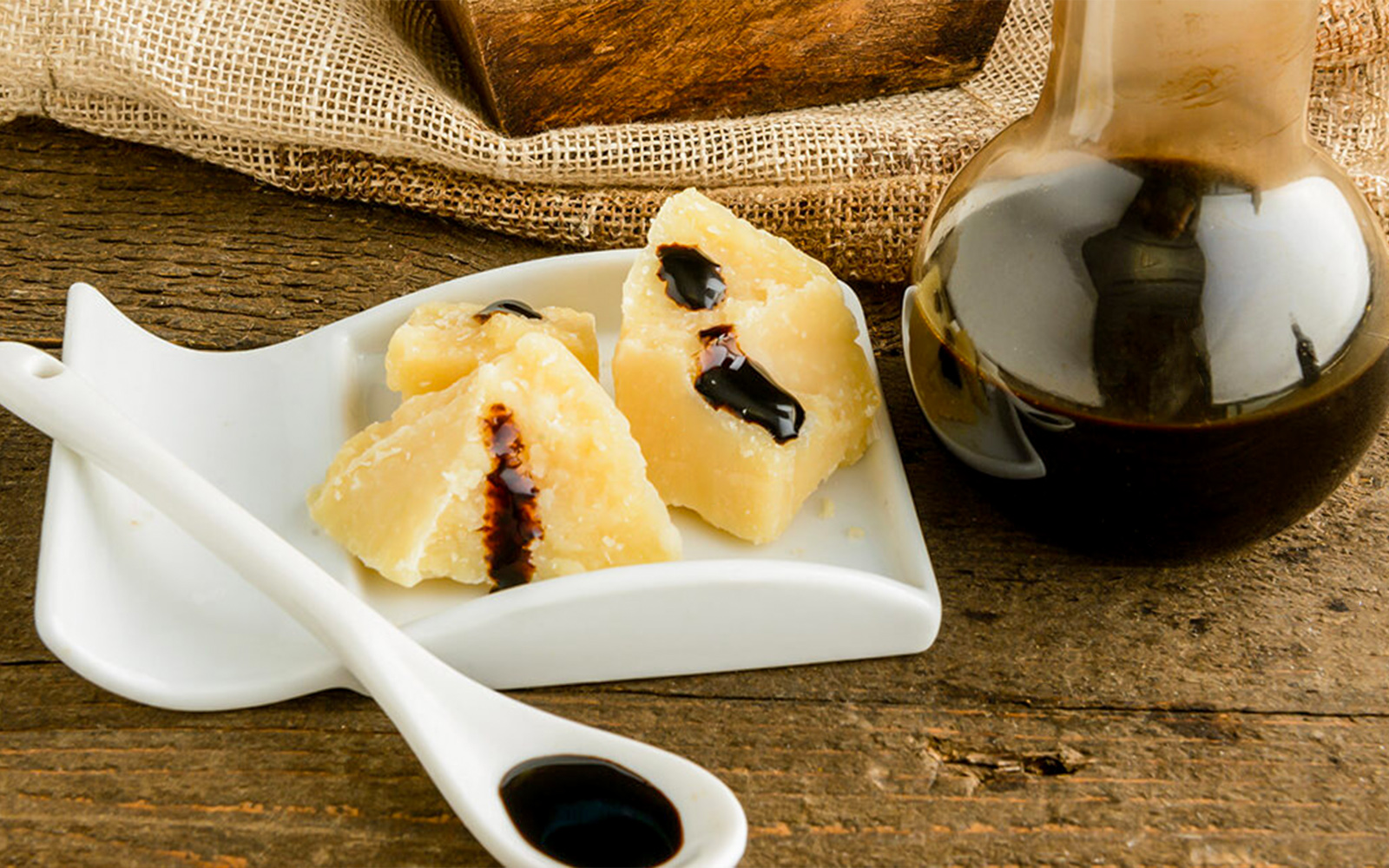 Cheese with balsamic vinegar and a bottle on a wooden table during a vinegar cellar tour.
