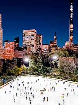 Skaters enjoying Wollman Ice Rink in Central Park with New York City skyline at night.