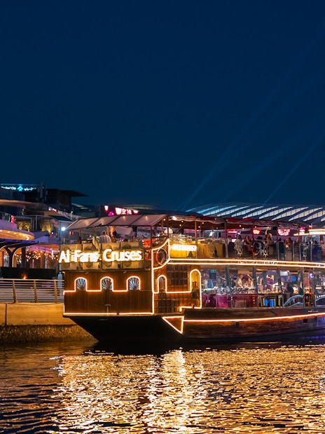 Dubai Canal cruise boat illuminated at night near waterfront buildings.