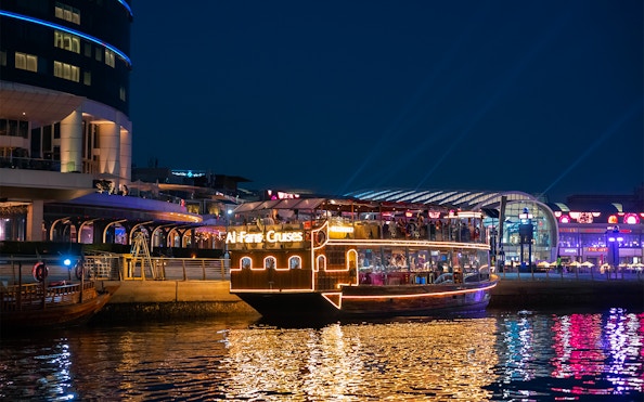Dubai Canal cruise boat illuminated at night near waterfront buildings.