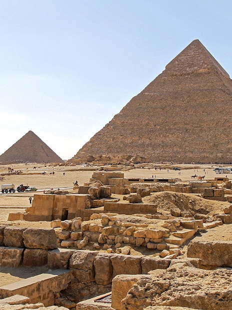 Pyramids of Giza on the Giza Plateau with tourists and camels in the foreground.