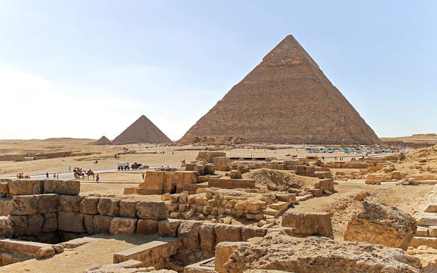 Pyramids of Giza on the Giza Plateau with tourists and camels in the foreground.