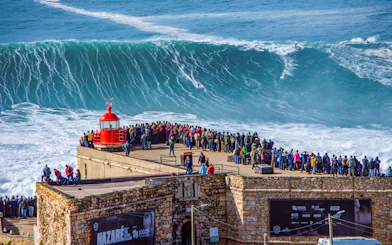 Crowd watching surfers ride giant waves at Nazaré, Portugal.