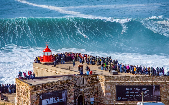 Crowd watching surfers ride giant waves at Nazaré, Portugal.