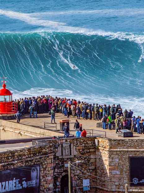 Crowd watching surfers ride giant waves at Nazaré, Portugal.