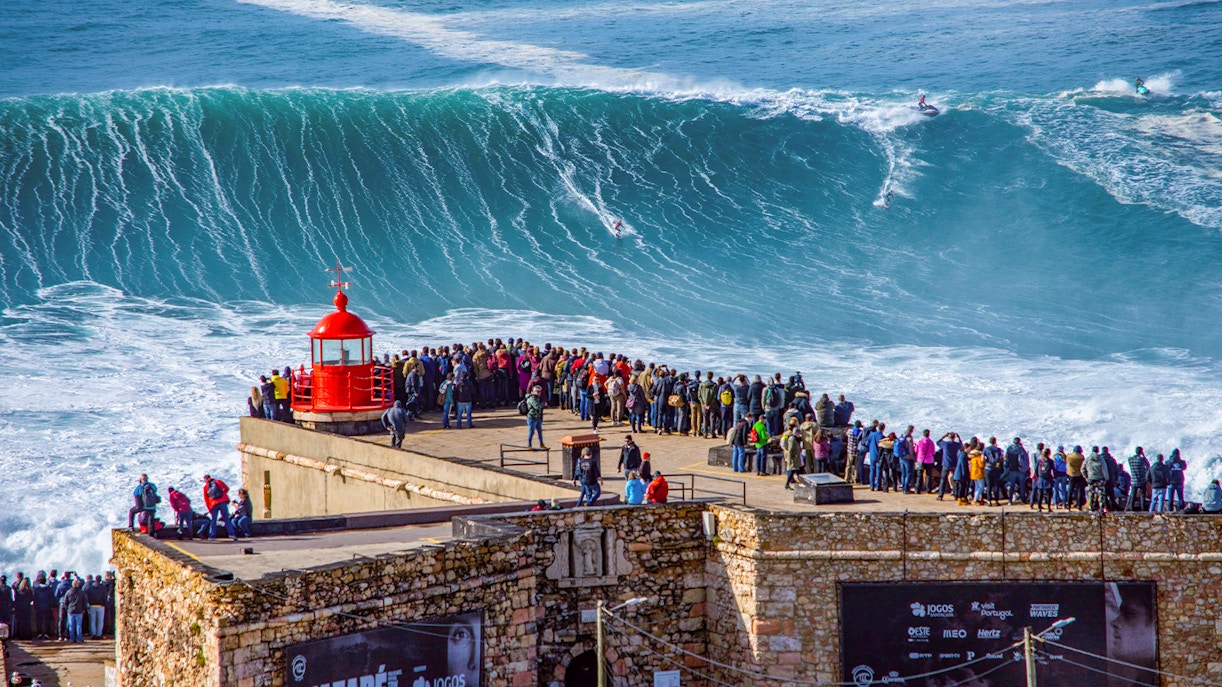 Crowd watching surfers ride giant waves at Nazaré, Portugal.