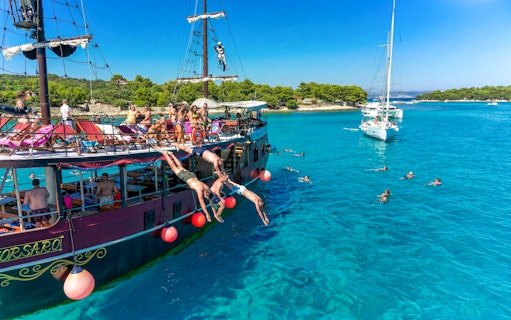 Tourists diving from a boat into clear waters near an exclusive beach resort.